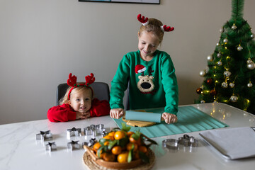 Two caucasian sisters preparing gingerbread cookies for Christmas at home