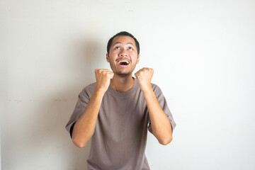 Overjoyed Asian young men in white isolated white background celebrating success with clenched fists