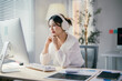 © Parichat - Focused businesswoman wearing headphones working at her desk in the office listening to music or participating in a virtual meeting