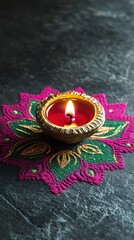 Low angle view, a single brass diya glowing atop a rich pink and green rangoli with swirling designs, resting on a dark grey surface, copy space, happy Diwali background, traditional, Indian 