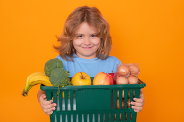 Wall Mural - Shopping grocery. Child grocery cart, isolated studio yellow background with copy space. Little shopper. Kid holding shopping basket. Fresh organic, vegetables and fruits in grocery food store