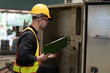 © amorn - Male electrician checking, repair, maintenance electric system board of CNC machine in factory. Male electrician engineer inspecting electric system during manufacturing process