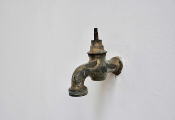 Old and aged rusty iron water faucet with missing valve handle part isolated on horizontal ratio white wall background.