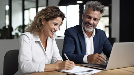 A photo of two business people smiling and working together on a laptop. 