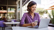© halo - a woman sitting at an outdoor cafe holding her phone and smiling, laptop on the table beside her, modern office in the background.