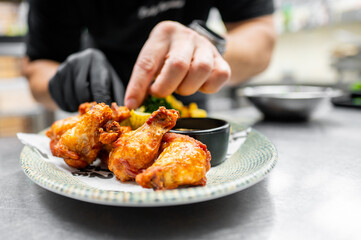 Wall Mural - A close-up of hands serving crispy fried chicken drumsticks on a white plate, garnished with fresh herbs and accompanied by a dipping sauce. Perfect for food blogs, menus, or culinary articles.