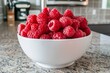 © Ilia K - Freshly picked raspberries in a white bowl on a kitchen countertop ready for use in summer recipes. Close-up