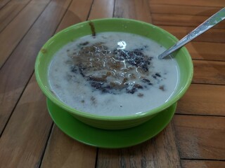 A traditional Indonesian dessert made by green bean porridge and black sticky rice with coconut milk topping in a green bowl