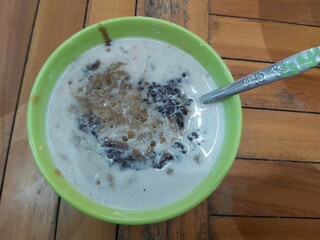 A traditional Indonesian dessert made by green bean porridge and black sticky rice with coconut milk topping in a green bowl