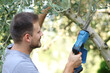 © Antonioguillem - Happy man pruning tree branch with electric saw