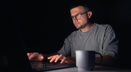 Young man works at the computer at night.