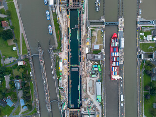 Topdown Aerial drone image of large cargo container ship carrier in lock sluice complex under construction in Brunsbüttel Germany at entrance of nord ostsee kanal or Kiel canal with small sailboat