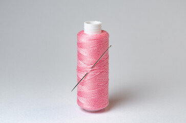 One single pink thread spool with needle on white background