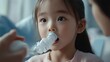 © Nathan - A young Asian girl watching intently as an adult assists her with a nebulizer treatment at home.