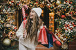 © polinaloves - Young beautiful womam enjoying Christmas shopping on a decorated street.