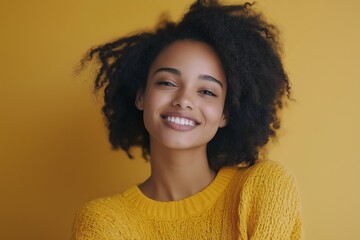 Wall Mural - A woman with curly hair is smiling and wearing a yellow sweater. She has a bright and happy expression on her face