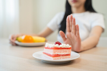 Wall Mural - Dieting young asian woman or girl use hand push out, dent sweet cake and control temptation for dessert.