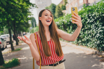 Wall Mural - Photo of lovely positive cheerful girl wear stylish clothes walk in town speak video call gadget summer time outdoors