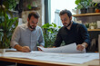© Ala - Two architects collaborate in a vibrant office, creatively exploring innovative designs on large blueprints during work hours