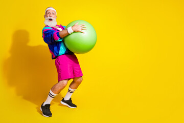 Wall Mural - Full length photo of cheerful positive mature guy dressed retro sport jacket holding fit ball emtpy space isolated yellow color background