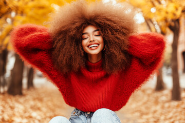 Wall Mural - A woman with curly hair is sitting on a bench in a park, wearing a red sweater