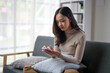 © apichat - A woman is sitting on a couch and looking at her cell phone
