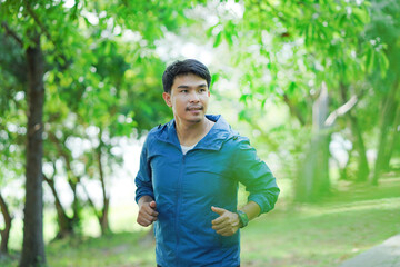 A man is running in a park with a blue jacket on. He is smiling and he is enjoying his run