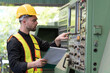 © amorn - Male engineer control CNC machine in factory. Male technician working and repairing or maintenance CNC machine with safety uniform, helmet in industry factory