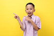 © ArvStd - Surprised asian boy standing while pointing sideways. Isolated on yellow background with copyspace