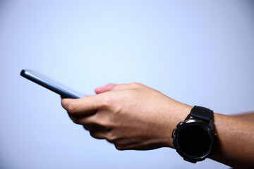 Wall Mural - Closeup of hand holding or using smartphone on blue background.