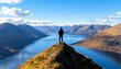 © Wimon - A lone figure standing on a mountain peak, overlooking a serene lake surrounded by majestic mountains under a bright blue sky.