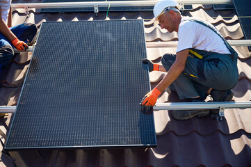 Wall Mural - Workers building solar panel system on rooftop of house. Two men installers in helmets installing photovoltaic solar module outdoors. Alternative, green and renewable energy generation concept.