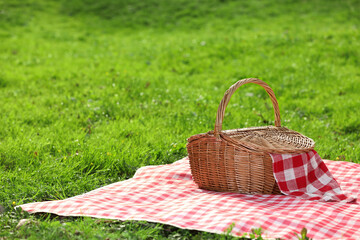 Wall Mural - One picnic wicker basket with checkered napkin and blanket on green grass. Space for text