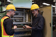 © amorn - Two male electrician checking, repair, maintenance electric system board of CNC machine in factory. Group of male electrician engineer inspecting electric system during manufacturing process