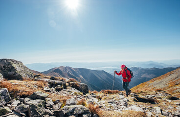 Backpacker woman in bright red jacket walking by mountain range using trekking poles with Liptov valley background, Western Tatras, Slovakia. Active people and European hiking tourism concept image.