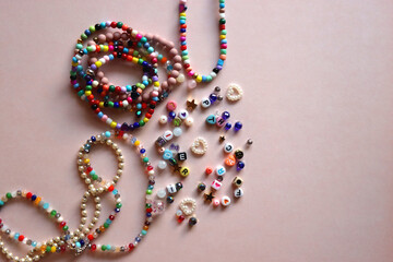 Colorful DIY necklaces, friendship bracelets and various plastic beads on pastel pink background. Flat lay.