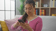 © Krakenimages.com - Young hispanic woman in glasses using smartphone in a cozy living room with bookshelf.