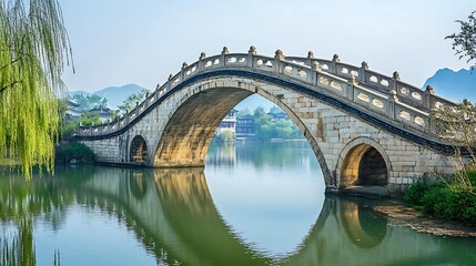 A stone arch bridge over a calm river reflecting the sky in a beautiful ancient Chinese village.