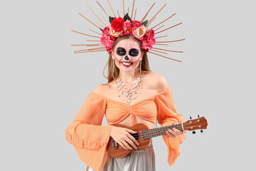 Wall Mural - Young woman with painted skull on her face playing guitar against grey background. Celebration of Mexico's Day of the Dead (El Dia de Muertos)