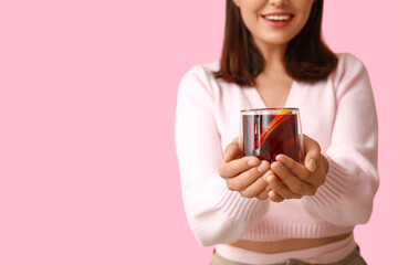 Wall Mural - Young woman with glass cup of hot mulled wine on pink background