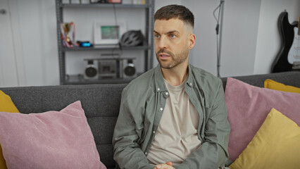 Wall Mural - Young hispanic man with beard sitting thoughtfully in a modern living room setting