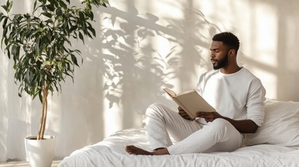 Aufkleber - A man sits comfortably on a bed, absorbed in reading a book. Sunlight filters through drapes, creating a warm atmosphere complemented by the presence of a thriving indoor plant nearby.