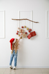 Poster - Cute little girl in Santa hat and Christmas advent calendar hanging on light wall