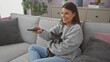 © Krakenimages.com - A young hispanic woman holding a chihuahua while sitting on a sofa in a cozy living room, using a remote control.