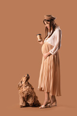 Poster - Beautiful pregnant woman with coffee cup and cocker spaniel on brown background