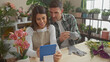 © Krakenimages.com - A woman and a man, florists, collaborate in a flower shop, surrounded by plants, using a tablet and preparing gloves for work.
