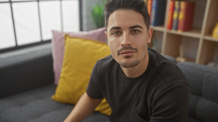 Handsome young hispanic man with beard sitting in a modern indoor room, exuding casual elegance.