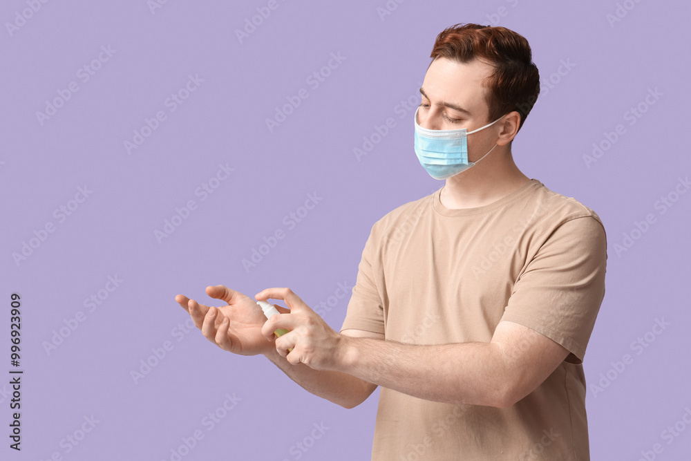 Young man with sanitizer on lilac background