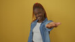© Krakenimages.com - A cheerful young african american woman extends her hand in greeting against a vibrant yellow background.
