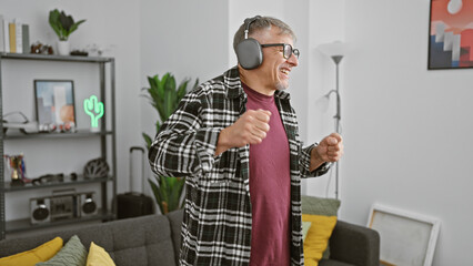 Canvas Print - A joyful senior man dances in a modern living room listening to music via headphones